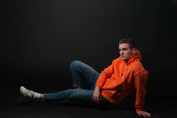 Man Modell Sitter Golvet Och Poserar Orange Sport Hoodie Isolerad — Stockfoto