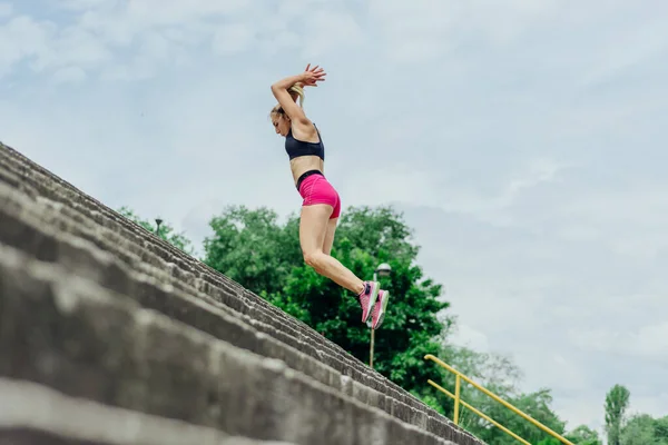 健康的なアスリートにフィット 階段を飛び降りるタイトなスポーツウェアの美しい女性 非常にやる気に見えるながらジョギングの前に暖まる — ストック写真