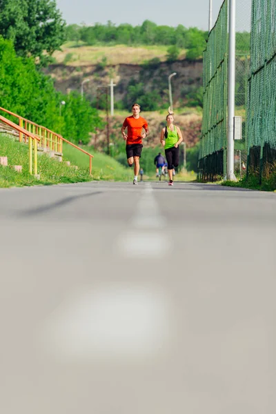 公園内の道路を走ったり走ったりする若い男女のアスリートたち — ストック写真