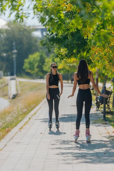 公園内の都市の通りに屋外に乗るローラースケートの2人の若いフィット女性のレビュー — ストック写真