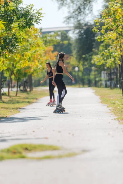 公園内の都市の通りに屋外に乗るローラースケートの2人の若いフィット女性のレビュー — ストック写真