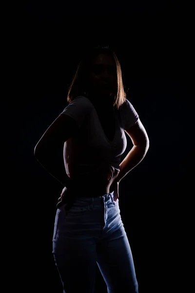 若いシルエットの女性は黒の背景に隔離された白いジーンズを着て — ストック写真