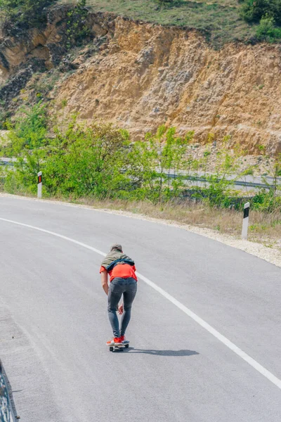 長いボードを速く運転しながら スピードタックを行い ボードをつかむ空の道路で下り坂に乗る男性の原因アジアのロングボーダー 赤いTシャツを着て緑の帽子と黒のジーンズ — ストック写真