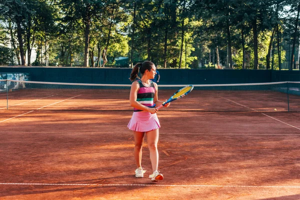 A young female tennis player serving on a clay court