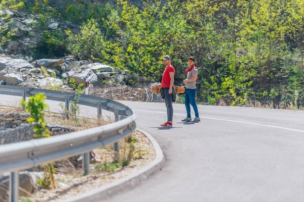 两名男性长板运动员在爬山和准备下坡滑行时 双手拿着长板 穿红色T恤 绿帽子和超酷太阳镜 — 图库照片