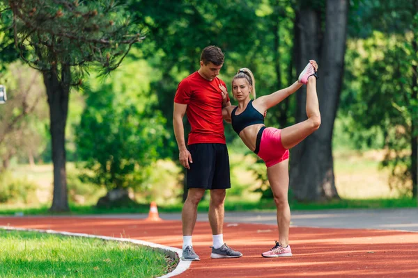年轻的男性运动员在他年轻的女伴跑完赛后伸腿时支持她 — 图库照片