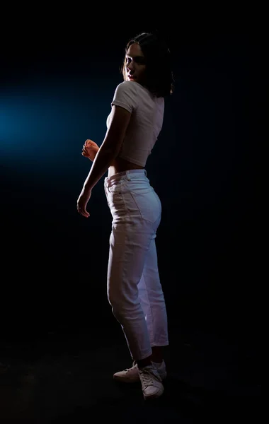 若いです幸せな美しいです女性Posingで新しいファッションホワイトジーンズとタンクトップ上に黒の背景 — ストック写真