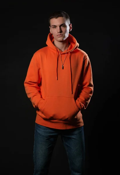 Close up portrait of a handsome male model looking serious while posing in orange hoodie inside a studio