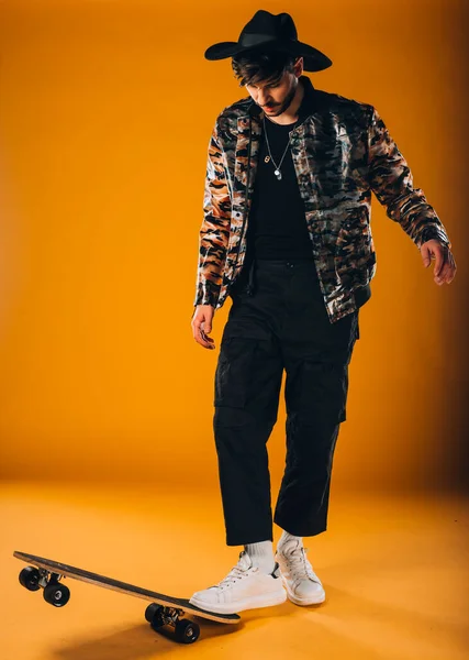 スケートボードに乗って現代的なスタイルの服を着て流行の若い男のスタジオボディショット — ストック写真