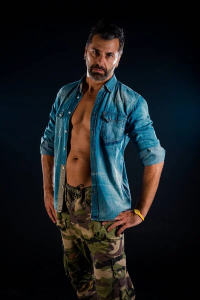 Attractive man posing in camouflage pants  and fancy unbuttoned jeans shirt