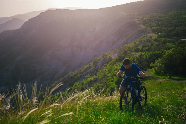 一个健康的山地骑车人把他的自行车推上了山坡 背景是森林 河流和山脉 景色令人叹为观止 日落时令人惊奇的绿色天性 — 图库照片