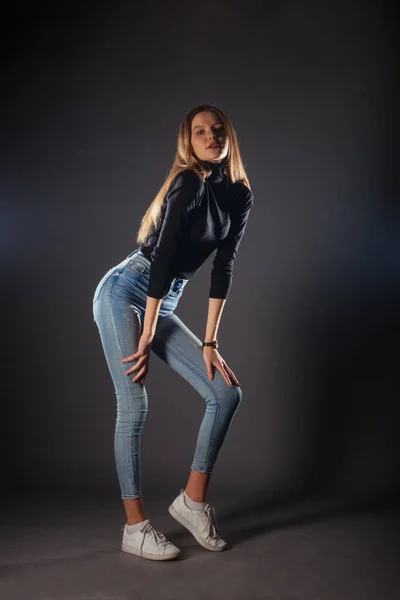サイド全身ポートレートの若い女性モデルで黒トップとジーンズポージングで1本足で前 — ストック写真