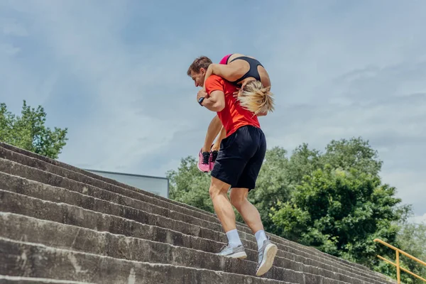 階段を駆け上がりながら肩に女性のトレーニングパートナーを運ぶ男性選手 — ストック写真