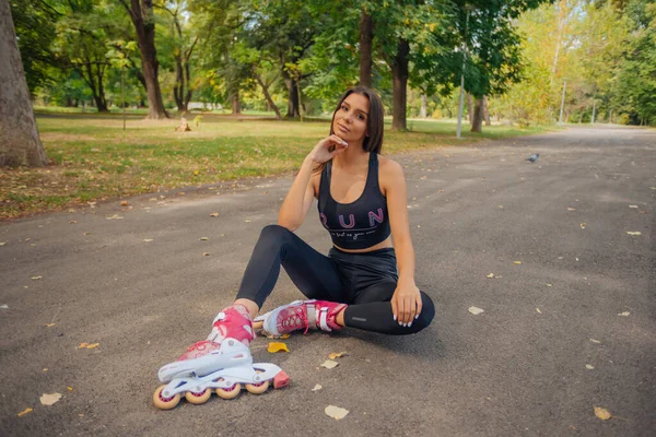 道路に座ってローラースケートでポーズをスポーツウェアで豪華な白人の若い女性の肖像画 — ストック写真