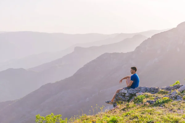 山の上に座って美しい景色を楽しみながら 青い川と素晴らしい山のラインを見下ろす冒険的な男 — ストック写真