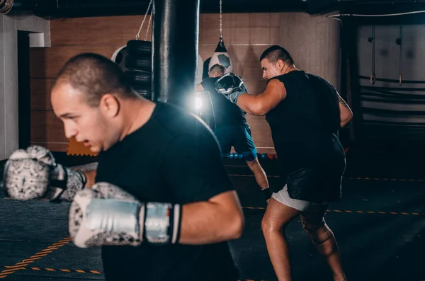 Male boxer training with punching bag in dark sports hall. Male boxer as exercise for the big fight. Boxer hits punching bag