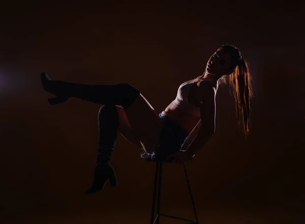 性感而充满热情的年轻女子坐在高椅子上 双腿向上摆姿势的高对比度轮廓 — 图库照片