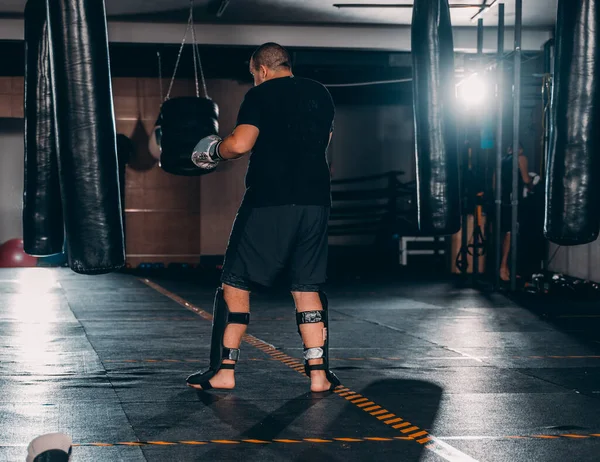 Silhouette male boxer hitting a huge punching bag at a boxing studio. Man boxer training hard