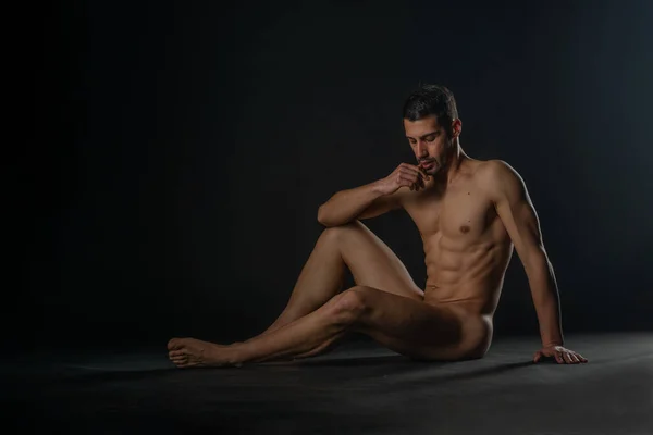 ファッションヌード写真の男モデルとともに魅惑的な姿座っ上の床に隔離されたスタジオ — ストック写真