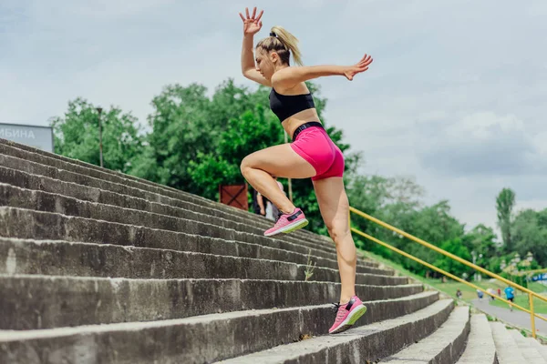健康的运动员 穿着紧身运动服的漂亮女人在楼梯上跳跃 在慢跑前热身 同时看起来很有动力 — 图库照片
