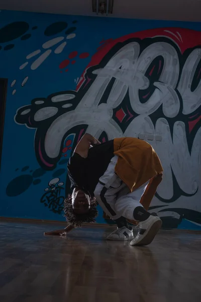 都市环境中年轻的黑人男子跳嘻哈风格 他穿着一件橙色的衣服 背景是涂鸦色的 — 图库照片