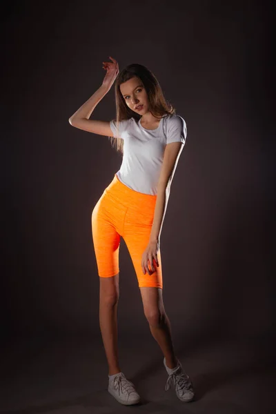 Hübsches Sportmädchen Mit Kurzen Orangefarbenen Leggings Posiert Isoliert Auf Dunklem — Stockfoto