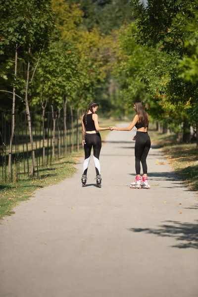 公園内の都市の通りに屋外に乗るローラースケートの2人の若いフィット女性のレビュー — ストック写真