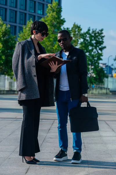 黒人男性と話をしながらオフィスビルの前で書類を持っているビジネス原因のアジアの女性の完全な長距離ビュー — ストック写真