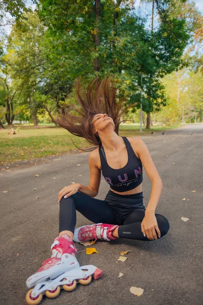 フィットスポーツ女性座っている道路にローラースケートと彼女の長いストレートの髪で遊ぶ — ストック写真