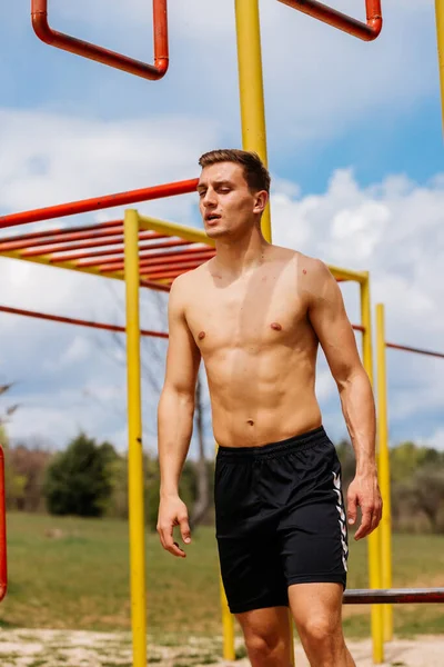 Joven atlético colgando de las barras en el gimnasio de calistenia al aire  libre sonriendo