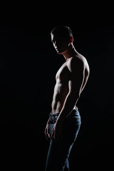 在黑暗的工作室里 一个穿着牛仔裤的性感的 赤身裸体的肌肉男的肖像 — 图库照片