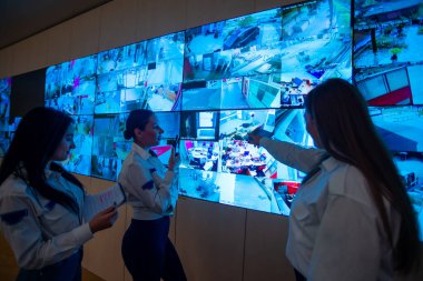 Security guards standing in front of a large CCTV monitor at the main control room while reading and discussing plans clipart