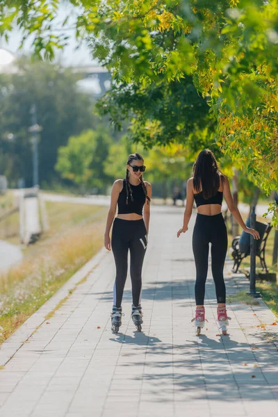 公園内の都市の通りに屋外に乗るローラースケートの2人の若いフィット女性のレビュー — ストック写真