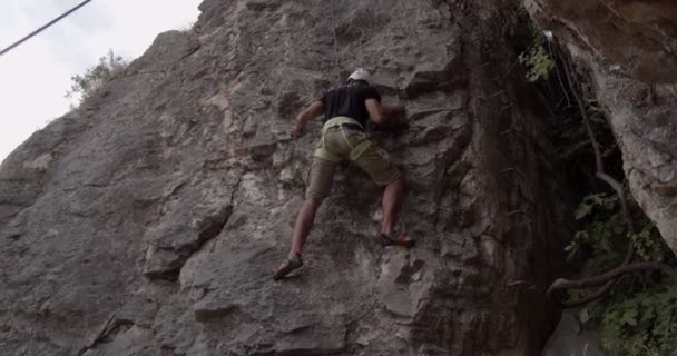 彼の次のステップについて多くのことを考えながらハンサムな男は大きな岩を登るフィット — ストック動画