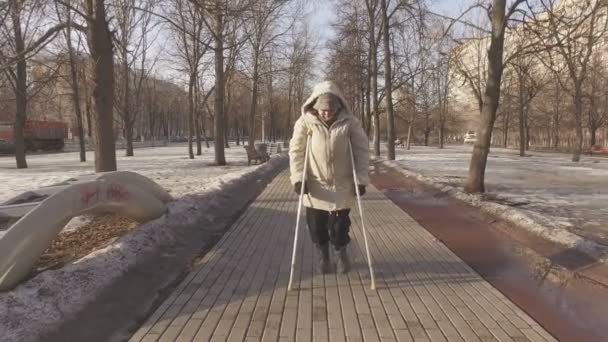 Rijpe vrouw op krukken in een stadspark — Stockvideo