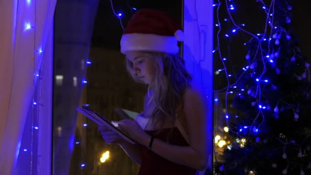 Chica rubia en sombrero de santa con una tableta — Vídeo de stock