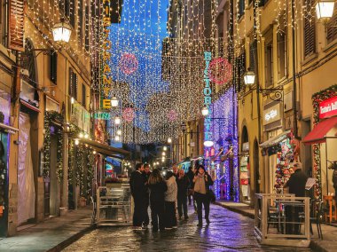 FLORENCE, İTALYA - 2 Aralık 2025: Turistler yağmurlu bir akşamda Noel ışıklarıyla süslenmiş Floransa 'nın güzel sokaklarında geziniyorlar