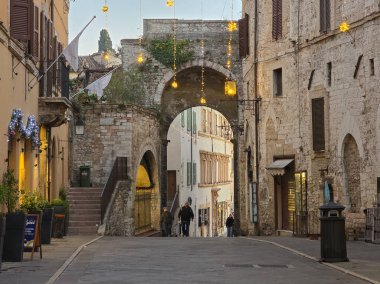 ASSISI, İtalya - 10 ARALIK 2025: Assisi, İtalya 'da dar, ortaçağ caddesi, şenlikli noel ışıkları ve iki büyük beyaz bayrakla süslenmiş