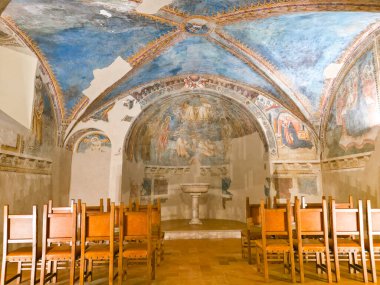 Spello 'daki antik şapelde canlı ortaçağ freskleri, kubbeli mavi bir tavan, merkezi bir vaftizsel yazı tipi ve sessiz bir yansıma ve dua için düzenlenmiş ahşap sandalyeler yer alıyor.