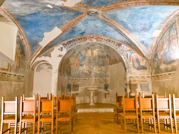 Spello 'daki antik şapelde canlı ortaçağ freskleri, kubbeli mavi bir tavan, merkezi bir vaftizsel yazı tipi ve sessiz bir yansıma ve dua için düzenlenmiş ahşap sandalyeler yer alıyor.