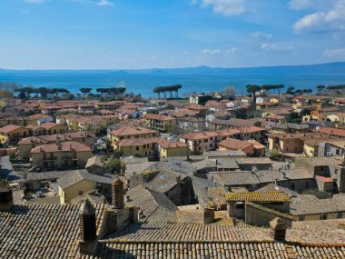 Arka planda kırmızı kil kiremit çatıları ve Bolsena Gölü olan Bolsena ortaçağ kasabasının yüksek açılı manzarası, Lazio, İtalya