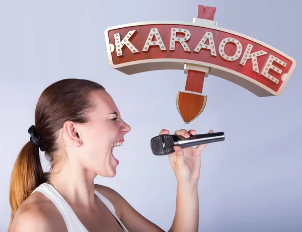 Meisje met een microfoon op de achtergrond van teken van karaoke. — Stockfoto