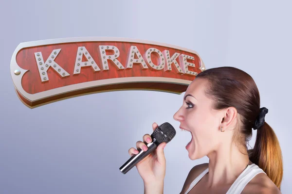 Meisje met een microfoon op de achtergrond van teken van karaoke. — Stockfoto