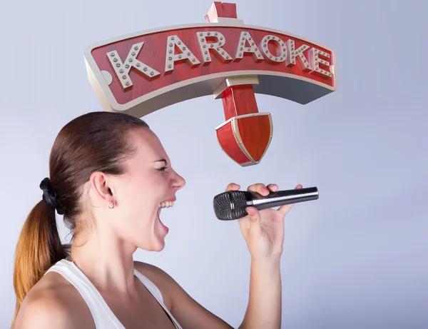 Flicka med en mikrofon på bakgrund av tecken på karaoke. — Stockfoto