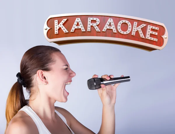 Meisje met een microfoon op de achtergrond van teken van karaoke. — Stockfoto