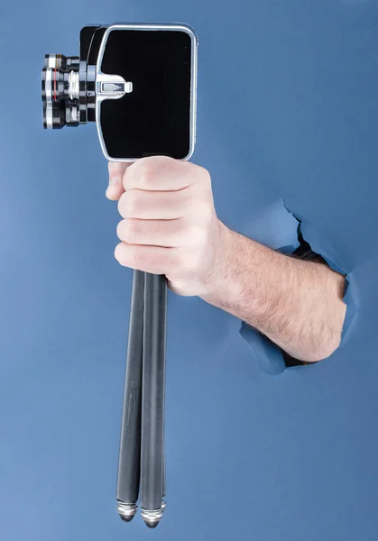 Male hand breaking through the blue paper background and holding retro camera — Stock Photo, Image