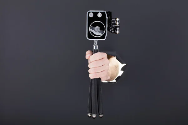 Male hand breaking through the black paper background and holding retro camera — Stock Photo, Image