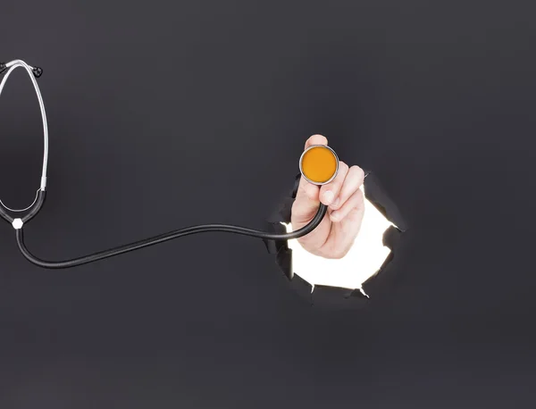 Mężczyzna ręcznie przebić na tle szarego papieru i przytrzymanie stetoskop — Zdjęcie stockowe