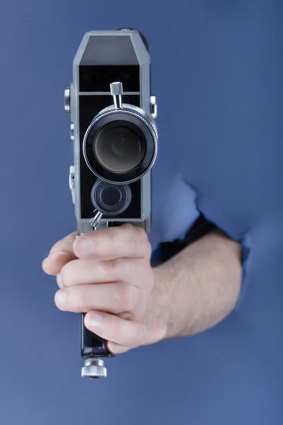 Mão masculina rompendo o fundo de papel azul e segurando câmera retro — Fotografia de Stock
