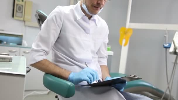 Der Zahnarzt schreibt in seinem Büro Notizbücher. — Stockvideo